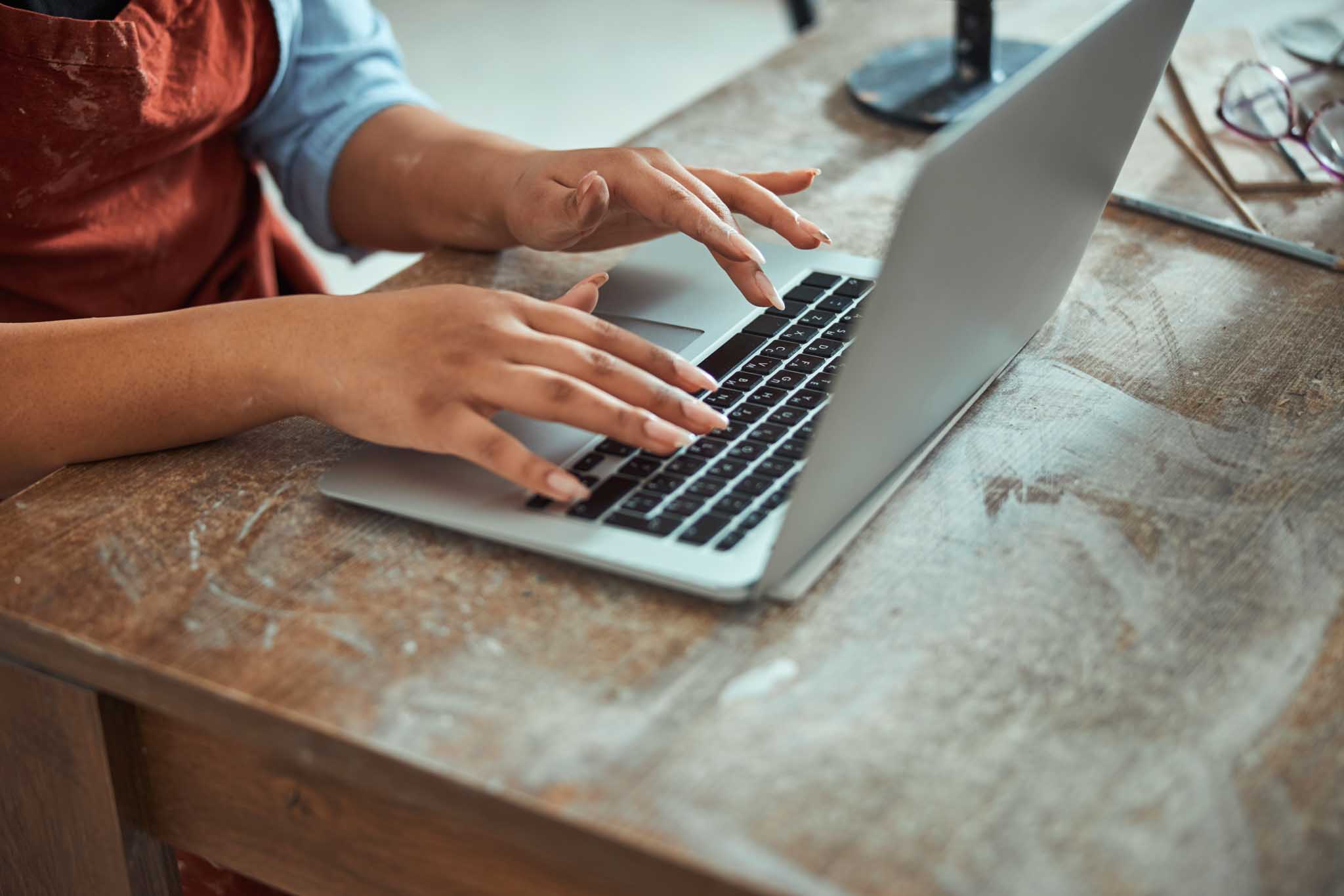 Close up of young woman sitting at the table and typing on her laptop to give to Engedi Church in Holland, MI.