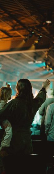 Woman holding a child with lifted hands worshiping at Engedi Church in Holland Michigan.